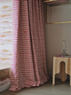 Hot pink scallop wave patterned curtain adding a bold, playful touch to a cozy interior space. The curtain’s vibrant design contrasts beautifully with a natural wooden table, creating a warm and inviting atmosphere. <br><br> Photography by Christopher Horwood.